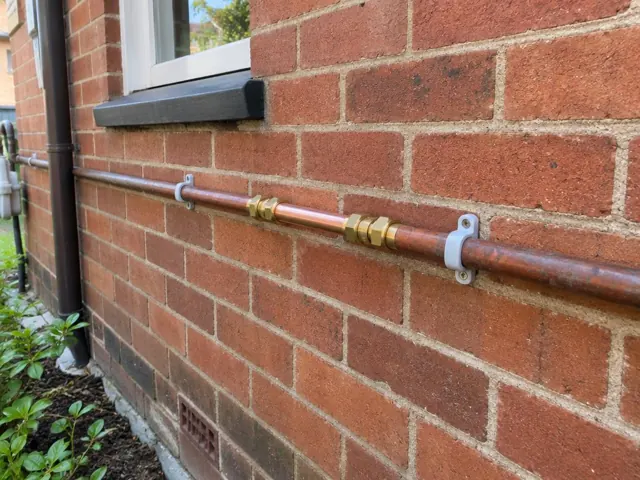 Repaired copper water pipe fixed along a brick exterior wall beneath a window in Cammeray