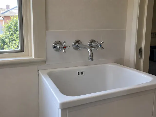 White laundry sink with chrome wall tap set and tiled splashback in a home interior in Naremburn